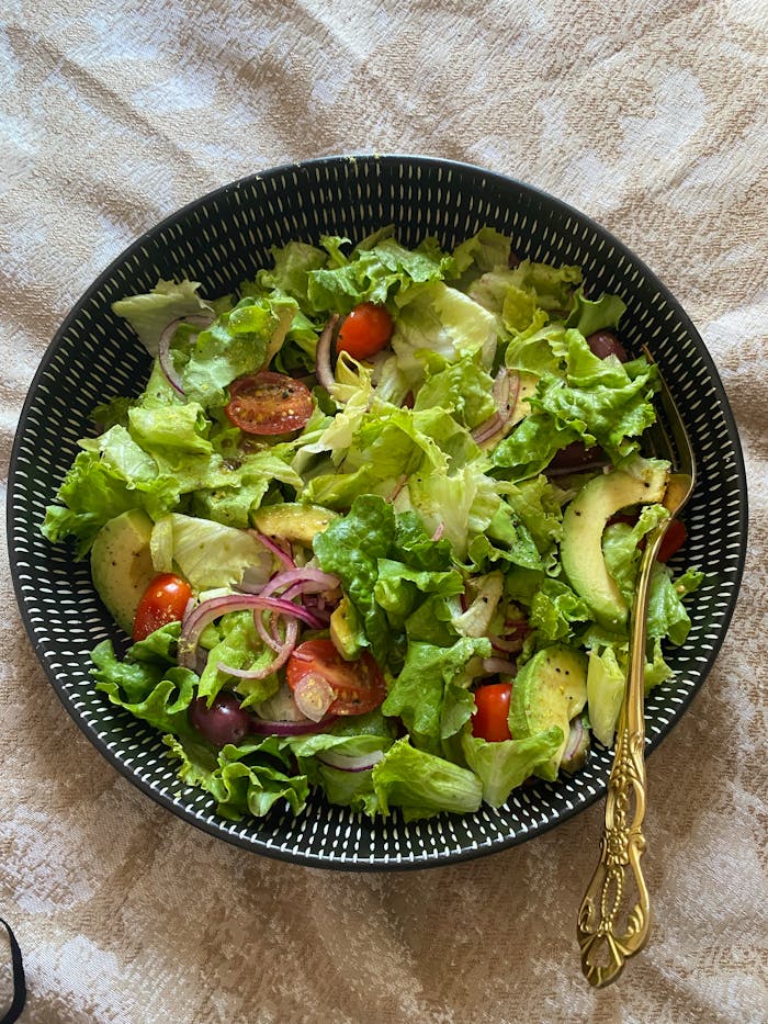 creative-03 Healthy mixed veggie salad with avocado, lettuce, olives, and tomatoes in a black bowl.